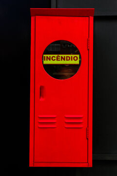 Caixa estreita de incêndio pintada de vermelho vivo com parta com visor e inscrição INCÊNDIO.