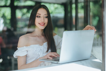 Portrait of beautiful smiling brunette woman sitting in a cafe with laptop outdoor.