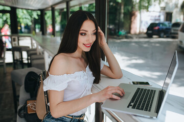 Portrait of beautiful smiling brunette woman sitting in a cafe with laptop outdoor.