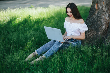 Young brunette woman, girl working with laptop, tablet and phone in green field, park with sunshine