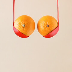 Oranges or tangerines in bold red ladles on isolated beige background. Minimal aesthetic abstract idea of boobs. Creative food concept. Breast and bra made with citrus fruit and kitchen equipment.