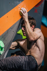 Fototapeta na wymiar A young, athletic guy with a beautiful inflated body climbs a bouldering in a climbing hall. Emotions on the face.