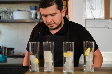 Latin man preparing soft drinks in a glasses with lemon and ice. Restaurant or bar.