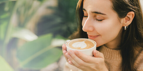 Young woman wearing sweater enjoying hot cappuccino outdoors.