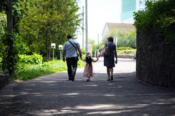 family walking in the park. mom dad and little girl walking holding hands. back view. daughter in a pink dress. friendly loving family concept, love. outdoor, walk in the fresh air, threesome