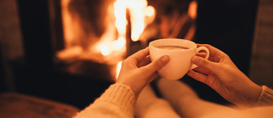 Woman drinkink hot cocoa sitting by the fire in front of cozy fireplace.