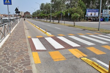 a wide two-lane road with a road for bicycles, a pedestrian crossing, yellow lines next to the...
