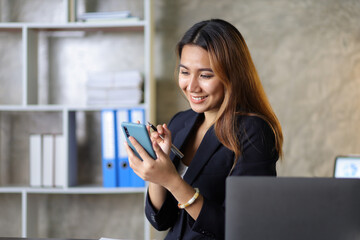 Attractive Asian businesswoman in office checking work schedule on smartphone.