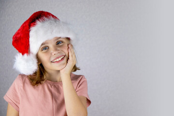 Portrait of a cute little girl with a wide smile in a santa hat on a light background. Merry Christmas, holidays