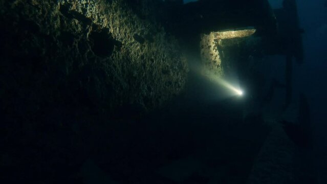 Diver exploring old sunken vessel underwater, shining with flashlight in darkness. Shipwreck discovery, ocean bottom scuba diving, old boat wreck undersea