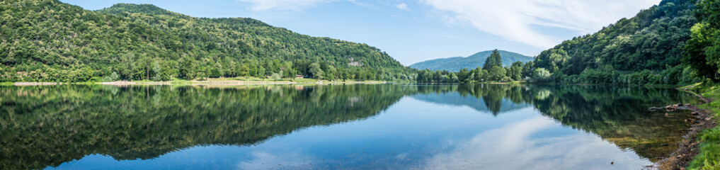 Panoramic view of mountains, trees and clouds perfectly reflected in a blue lake
