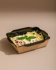 Bolognese pasta in cardboard box with basil closeup for delivery service.