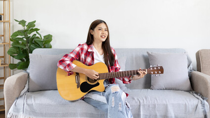 Asian female artist playing the guitar and singing happily in the living room, Relaxation with music therapy, Spending free time with music, Joy of playing music, Acoustic guitar.