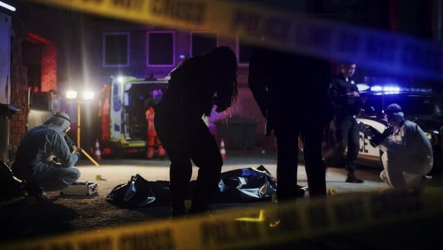 Zoom Out of "Do-not-Cross" Tape: Crime Scene Investigation Team Working on a Murder Case at Night. Police Receiving a Tip on a Dead Body in a Back Street. Forensics and Detectives Solving the Case