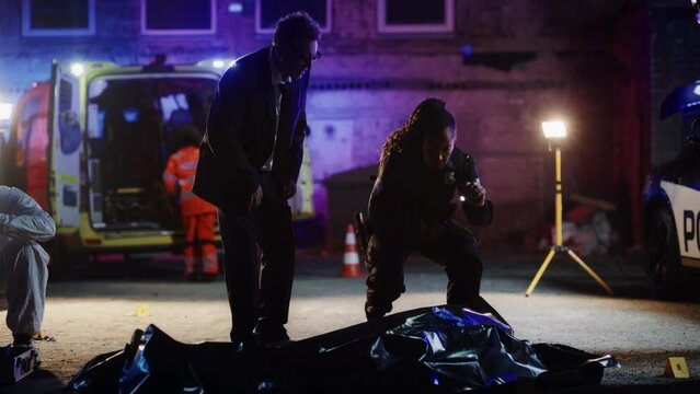 Team of First Responders Arriving at a Murder Scene in a Back Alley. Police Officer and Detective Making Preliminary Assumptions of the Potential Events of the Night and Consider the Evidence and Body