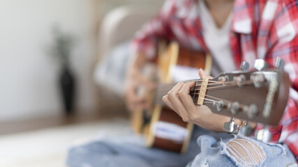 Woman practicing or learning to play guitar and practice using his fingers to hold guitar chords while looking at music notes with intention, Taking advantage of free time, Relax during free time.
