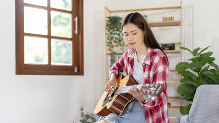 Asian female artist playing the guitar and singing happily in the living room, Relaxation with...
