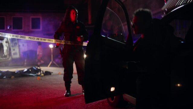 Cinematic Shot: Lieutenant Arriving At a Crime Scene, Crossing the Yellow Tape, Listening to Briefing from First Responder Officer. Detective Checking the Body Bag. Forensics Team Gathering Evidence