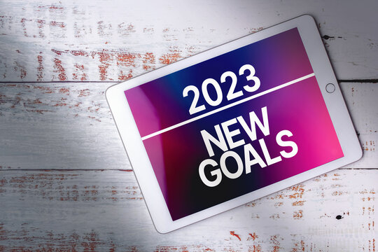 Top view of white wood desk with digital tablet and new goals text on screen with copy space. Planning new goals to reach this next year. Achievements, aspirations and wishes.
