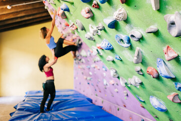 Sportswoman climbing wall with help of trainer