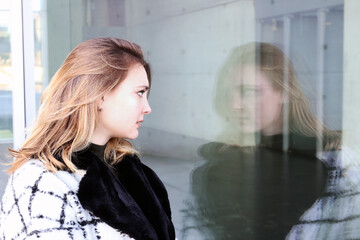 young woman standing outside and looking at her reflection at window