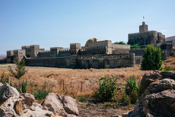 View of the medieval Akhaltsikhe Castle in southern Georgia. It's a hot summer day with blue skies. The grass is yellow. In the foreground are rocks.