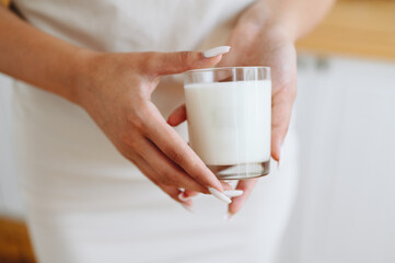 Woman in Home Clothes Holds White Candle with Wooden Lid in Her Hands. Blurred Background. Scented Candle Handmade for Comfort at Home close-up.