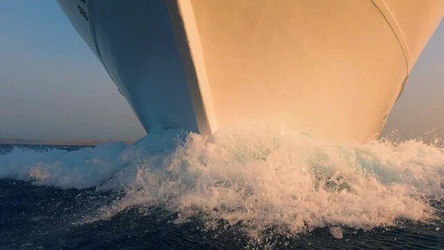 Boat prow and white foam water splashes close up front side view. Yachting, ocean sailing, sunrise sun light on vessel forepart, sailboat bow closeup