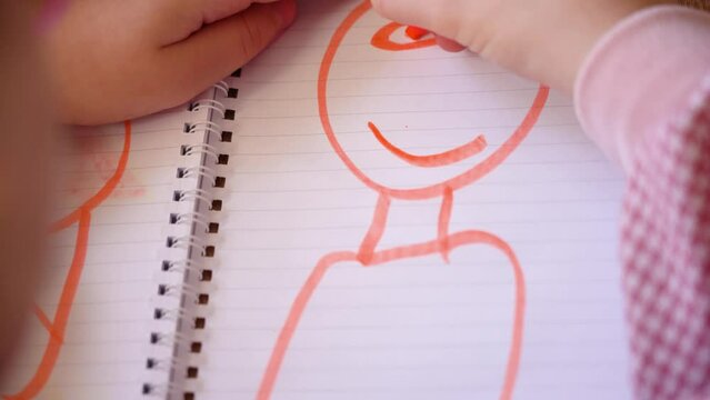 Child draws his mother in notebook with an orange marker. 