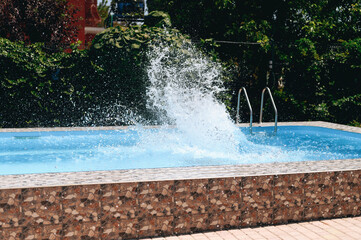Splashes of water in the pool on the background of a green garden