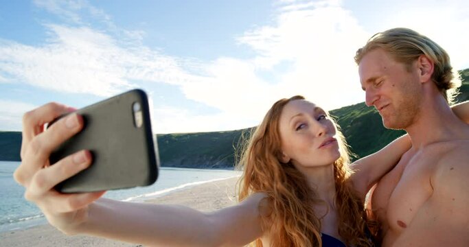 Couple, beach selfie and kissing for romance, love and happy with smartphone, bonding and care outdoor. Woman, man and phone for photo by ocean, water and vacation to relax, rest and social media app