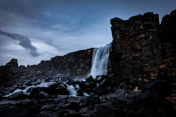 Oxararfoss waterfall, surrounded with black volcanic rocks in Thingvellir, Iceland. Dark, moody...