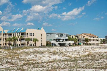 Grasses on a white sand dunes near the fenced residential buildings against the sky in Destin, FL
