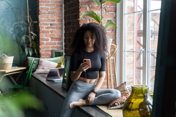 Black woman with African curls using smartphone at home or cafe indoors. Communication with friends of relatives. social media. Video photo content. Comfort relationships. Freelance