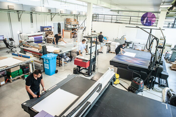 In a large modern printing plant, operators work on various types of machines for printed material