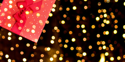 Red gift box with a bow on a dark background with golden bokeh. Banner format.