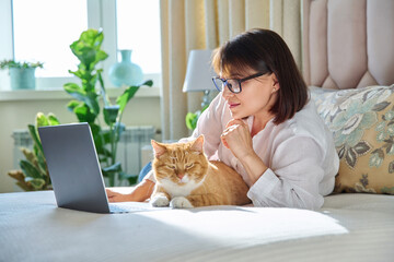 Middle aged woman at home on couch with laptop and cat