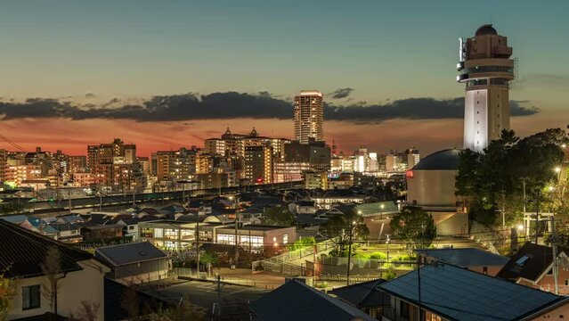 Clouds move over small city and clock tower as trains zip by at sunset