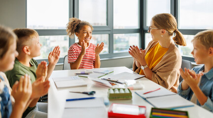 Teacher and joyful students celebrate   successful completion of collective school work in a bright classroom