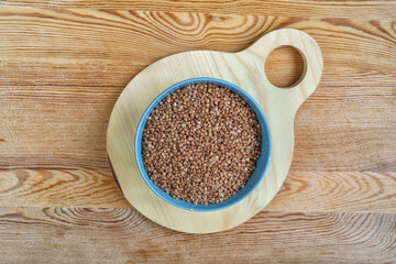 Buckwheat in a bowl on wooden background, top view.
