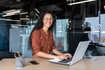 Young beautiful hispanic woman working inside modern office, businesswoman smiling and looking at...
