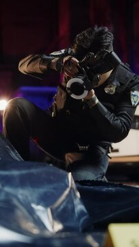 Vertical Shot: Asian Man from Forensics Team Taking Photos of Evidence and Victim's Body in a Crime Scene at Night. Professional Investigator Working to Solve the Case of Potential Premeditated Murder