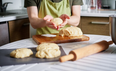 Male chef baker in green apron making dough balls with wooden cutting board on background. Working at home kitchen concept, homemade baking. High quality image
