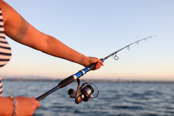 Woman holds spinning rod in her hands and fishing in sea.