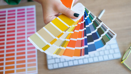 Woman's hand holds color swatches over her desk.