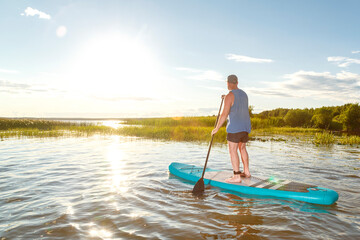 a man in shorts stands with a paddle on a sup board at sunset in the water.