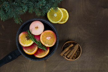 Mulled wine with pieces of orange and apples in a black ladle on a wooden background.