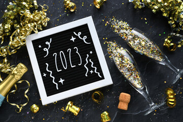 Welcoming 2023 New Year - flat lay champagne glasses bottle gold glitter confetti golden streamers