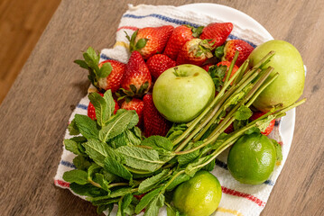 Fruits lie on a wooden table: strawberry, apples, lime, mint