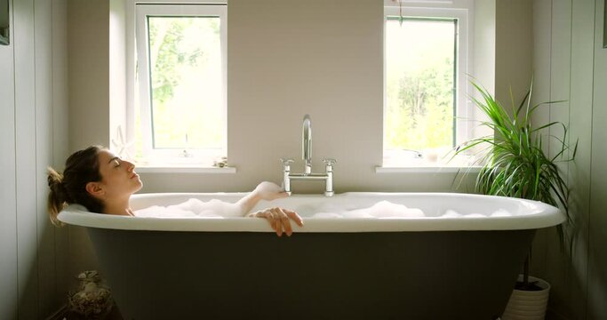 Woman, bathtub and relax in bathroom home for hygiene or health. Wellness, cleaning and relaxed female bathing in bubble bath for stress relief, skincare or body care and enjoying time alone in house